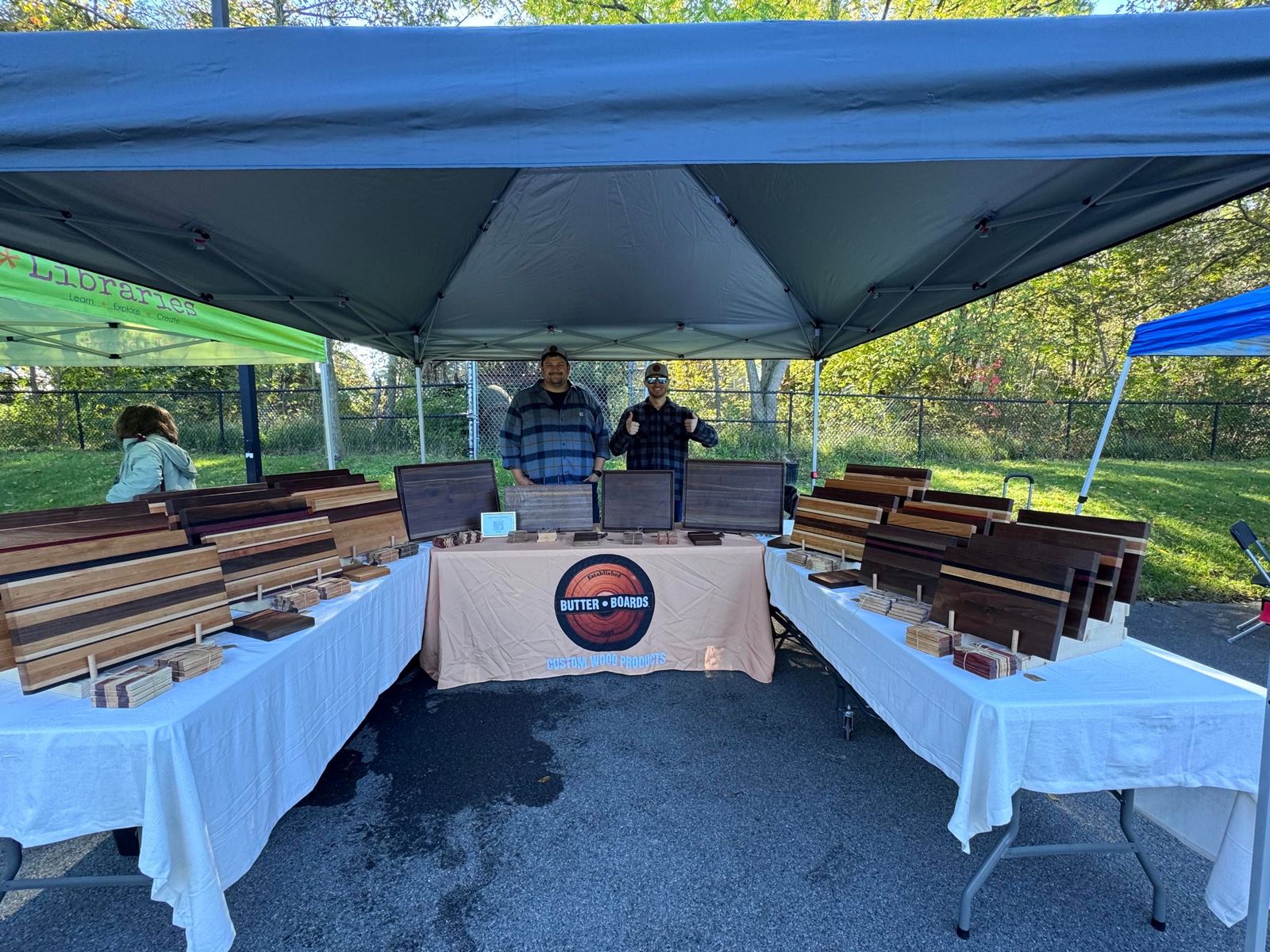 Ryan and Greg of Butter Boards at their craft show booth, with tables full of cutting boards